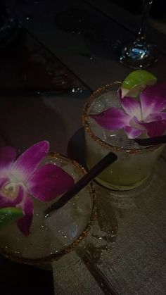 two cocktails with flowers in them sitting on a table