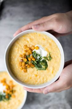 two hands holding a bowl of corn and cheese soup