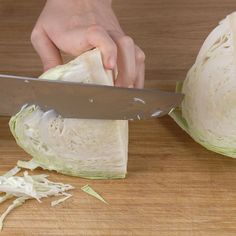 a person cutting up cabbage on top of a wooden table next to a large knife