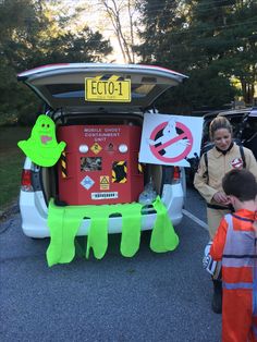 two children standing in front of a car with its trunk open and signs on the back