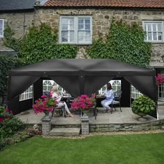 two people sitting at a table under a black awning in front of a house