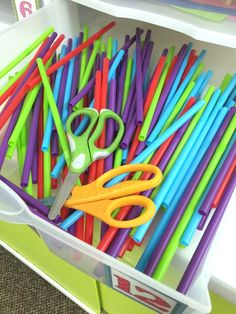 several pairs of scissors are sitting in a bin filled with plastic straws and colored sticks