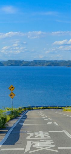 an empty road near the ocean with a yellow sign pointing to it's left