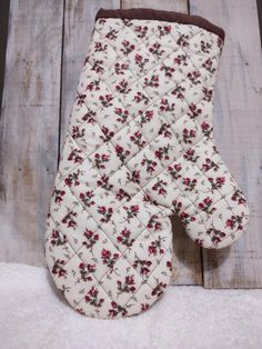 the oven mitt is made out of fabric and has flowers on it, sitting on a wooden surface