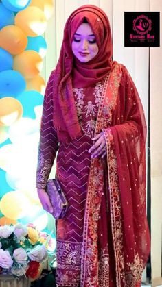 a woman wearing a red and purple outfit standing in front of a flower pot with flowers