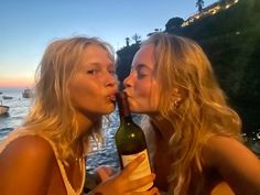 two beautiful young women sitting next to each other with a bottle of wine in front of them