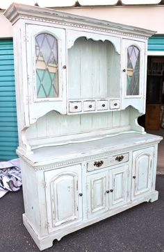 an old white china cabinet with glass doors on the top and bottom, in front of a blue garage door