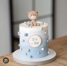 a blue and white baby shower cake with a teddy bear sitting on it's top