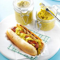 a hot dog with mustard and ketchup on a plate next to two jars