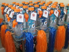 many orange and blue water bottles are lined up on a table with tags attached to them