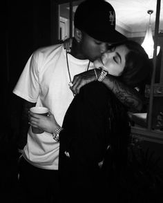 a man kissing a woman while holding a cup in front of her and wearing a baseball cap