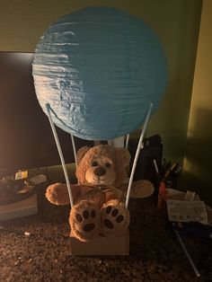 a teddy bear sitting on top of a box under a blue balloon