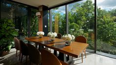 a dining room table with chairs and vases on it in front of large windows