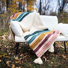 a white couch with a multicolored blanket on it in front of some trees