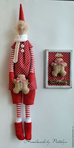 a red and white christmas doll next to a wall hanging with a teddy bear on it