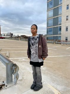 a woman standing in an empty parking lot next to a metal railing and building with windows