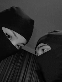 two people in black and white are covering their faces with head coverings, looking at each other