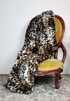 a leopard print fur blanket sitting on top of a wooden chair next to a wall