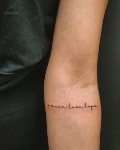 a woman's arm with the words never laugh on it, in cursive font