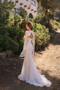 a woman in a white wedding dress standing on a dirt road near bushes and trees