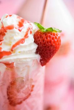 a strawberry milkshake with whipped cream and strawberries on the rim, sitting on a pink surface