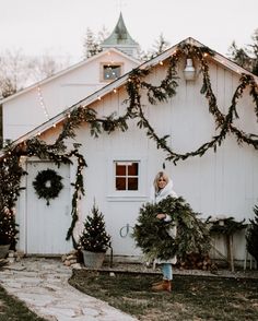 a woman standing in front of a white house with christmas wreaths on the door