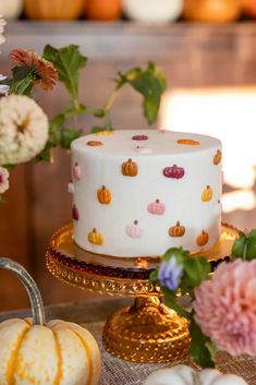 a white cake sitting on top of a wooden table next to flowers and pumpkins