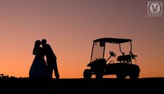 a man and woman standing next to each other near a golf cart in the sunset