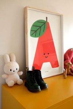 two stuffed animals are sitting on a yellow shelf next to a framed letter with a green leaf