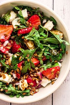 a salad with strawberries, spinach and feta cheese in a white bowl