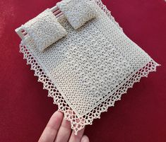 a hand is holding a crocheted doily with two pillows on top of it