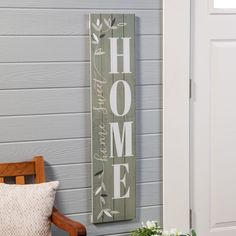 a wooden sign hanging on the side of a house next to a chair and potted plant