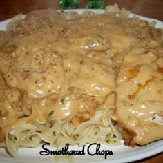 a white plate topped with meat covered in gravy and noodles on top of a wooden table