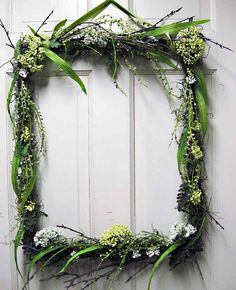 a wreath made out of branches and flowers hanging on a door frame with greenery