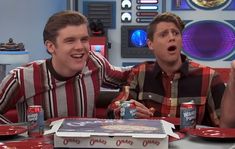 two young men sitting at a table with pizza and sodas in front of them