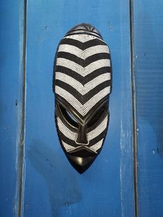 a black and white mask hanging on the side of a blue wooden door with horizontal stripes