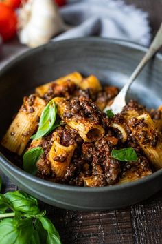 a bowl filled with pasta and meat on top of a wooden table next to vegetables