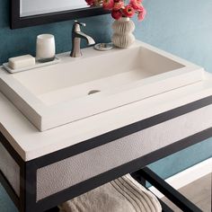 a bathroom sink sitting under a mirror next to a vase with flowers on top of it