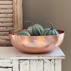 a large metal bowl filled with green gourds on top of a wooden table