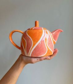 a hand holding an orange and white teapot