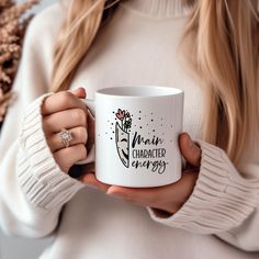 a woman holding a white coffee mug with the words main character energy on it in front of her