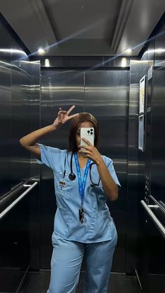 a woman in scrubs taking a selfie with her cell phone at the elevator