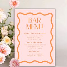 a pink menu card with gold foil lettering on it next to flowers and a vase