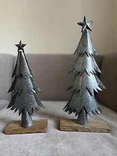 two metal christmas trees sitting on top of a wooden stand in front of a couch