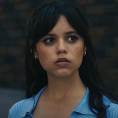 a close up of a person wearing a blue shirt and gold necklace with an evil look on her face