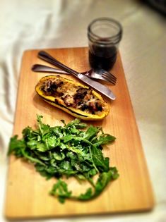 a wooden cutting board topped with greens next to a jar of sauce and utensils