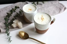 two mugs filled with liquid sitting on top of a table next to a spoon