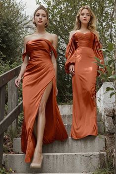 two women in long dresses walking up some steps together and one is wearing an orange dress