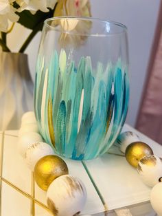 a glass with some paint on it sitting on a table next to gold and white balls