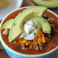 a bowl of chili with avocado, sour cream and cheese on the side